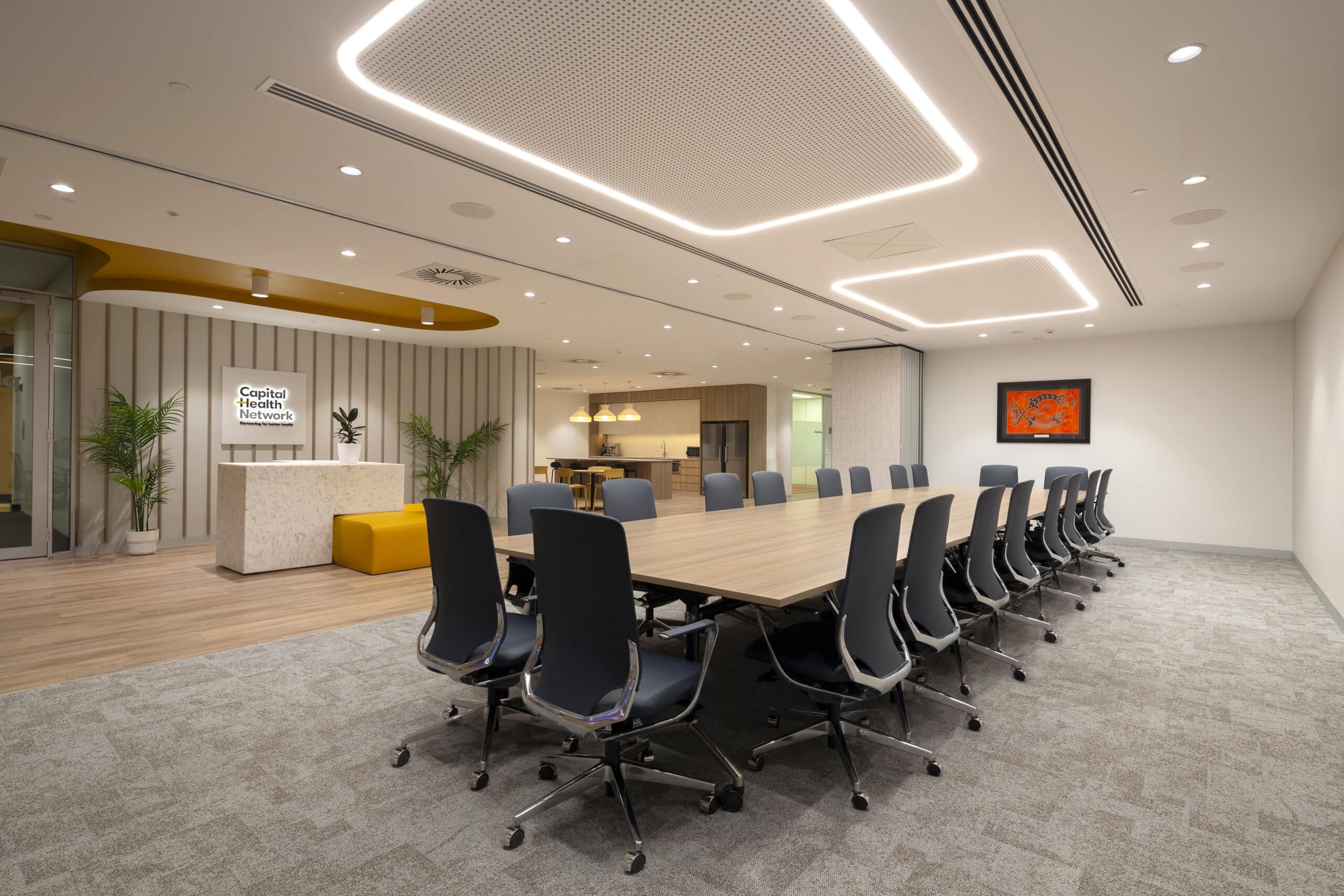 Modern boardroom with a long conference table, ergonomic chairs, large windows, and minimalist design, featuring neutral tones and sleek finishes.