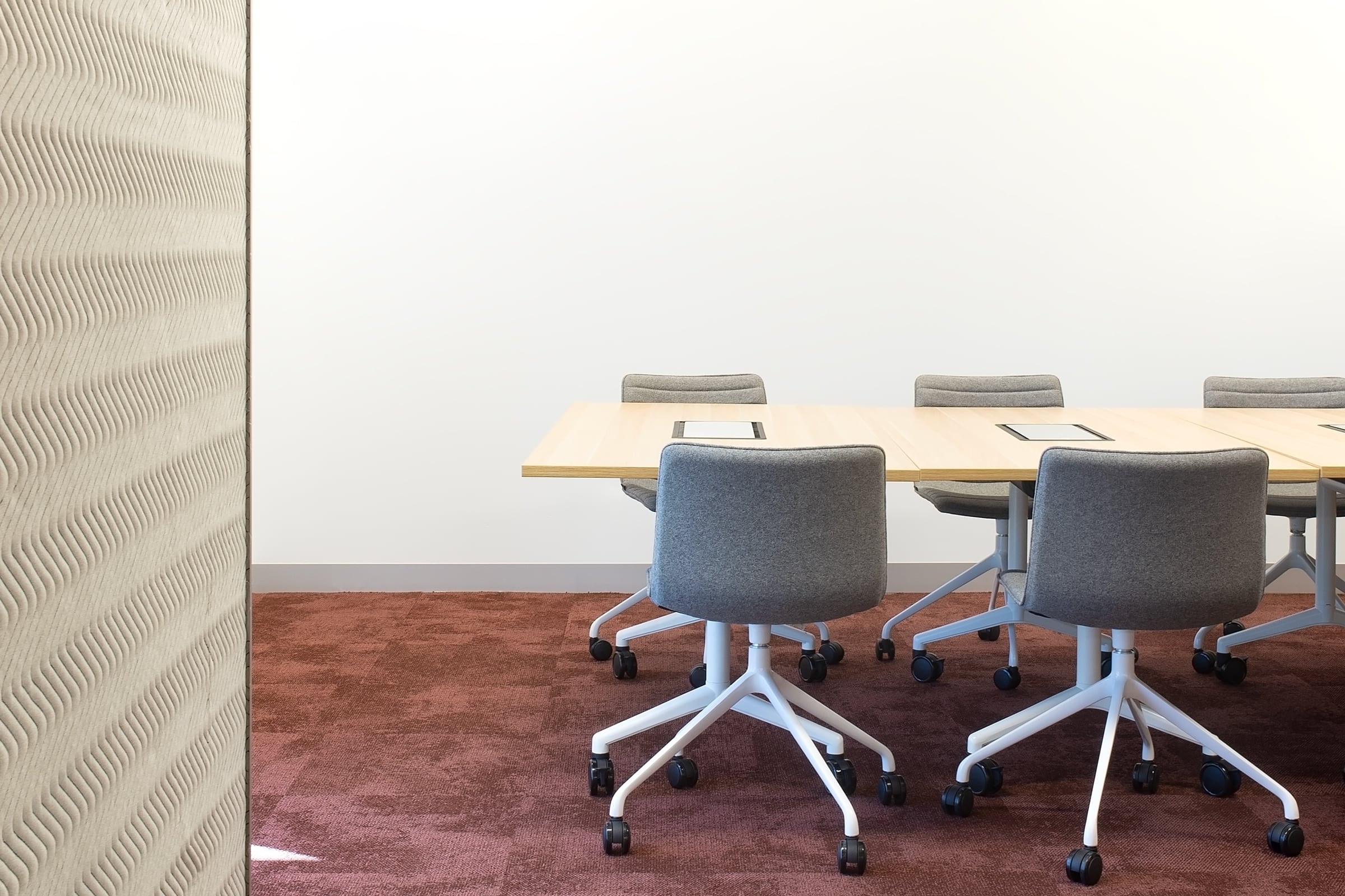 Meeting room with timber table, upholstered chairs, red carpet tiles, and textured acoustic wall panel for sound control.