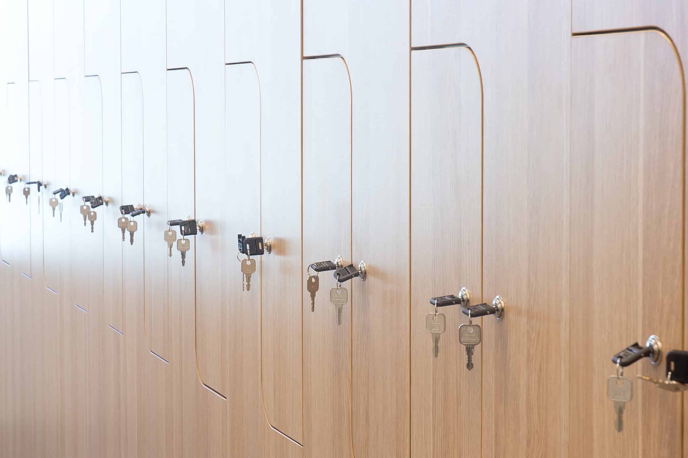 Row of timber personal lockers with integrated key locks arranged along a clean office corridor wall.