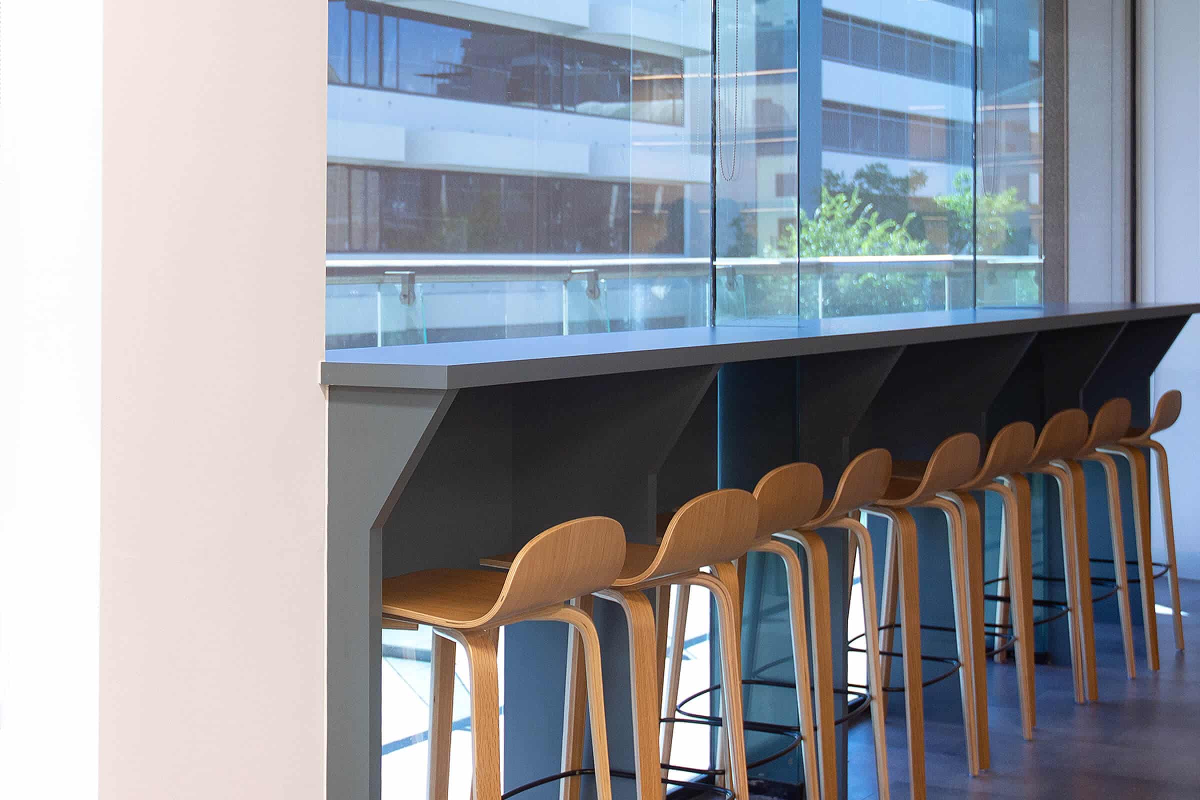 High bar seating with timber stools positioned along a window ledge overlooking an internal office atrium.