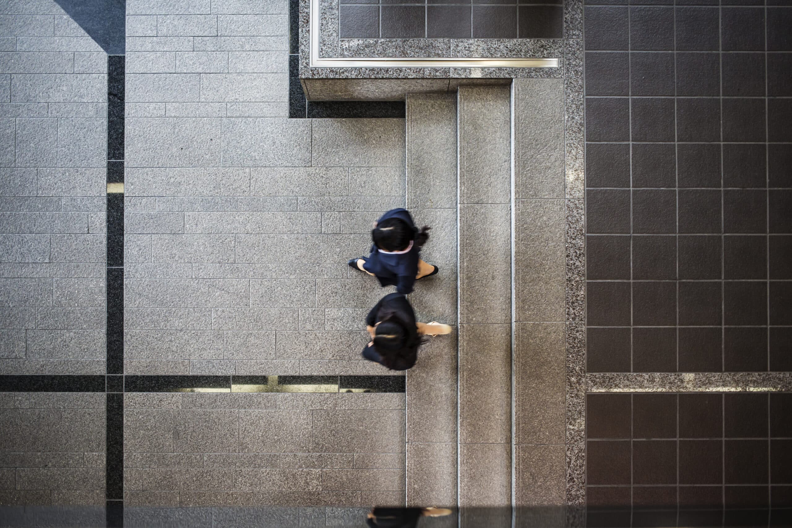 Overhead view of people walking through a modern workplace with patterned stone flooring and clean architectural lines.